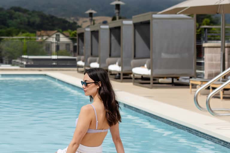 Woman in sunglasses at modern resort pool with white cabanas and mountain views in background