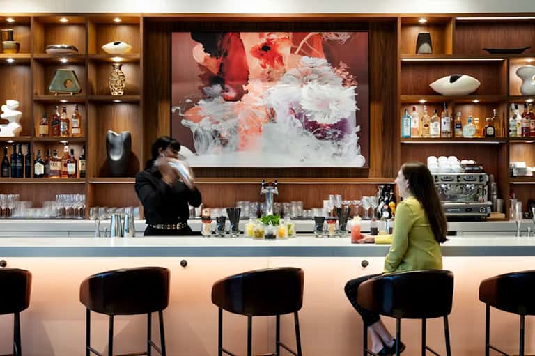 Hotel bar with wooden shelving, liquor bottles, modern bar seating, and abstract artwork