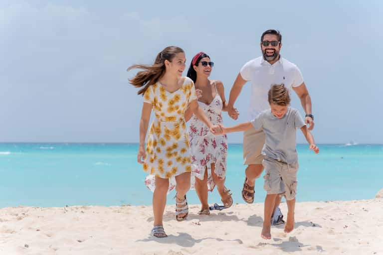 Family of four running on sandy beach with turquoise ocean water in background