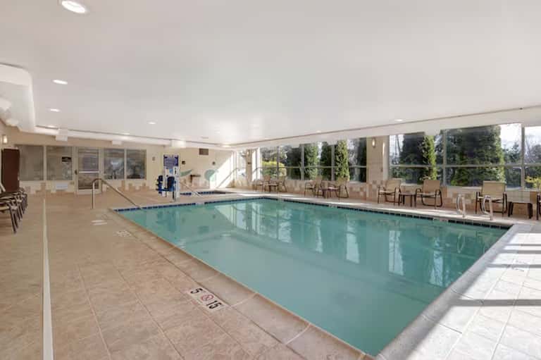 Indoor lap pool with beige tile flooring, floor-to-ceiling windows, lounge seating, and modern architecture