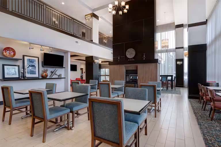 Contemporary hotel lobby with two-story fireplace, blue upholstered chairs, wood accents, and high ceiling