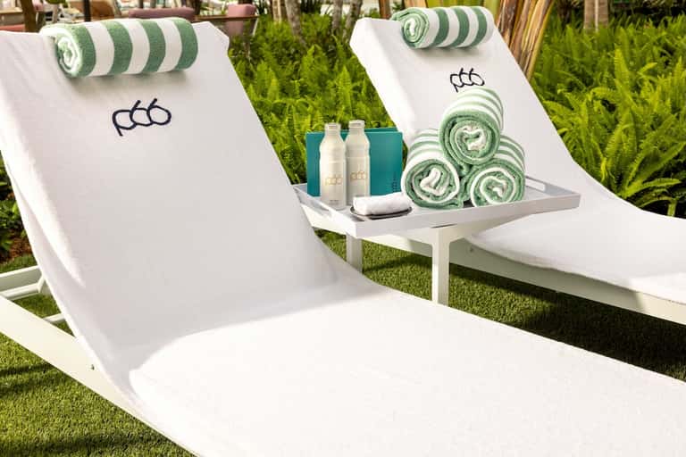 Luxury lounge chairs with branded towels, rolled towels with green stripes, and branded amenity bottles