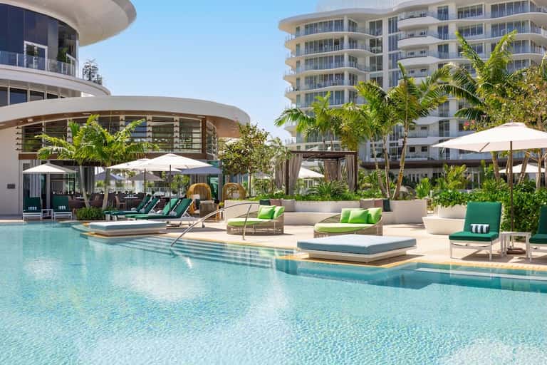Resort pool area with loungers, umbrellas, tropical landscaping, and modern buildings