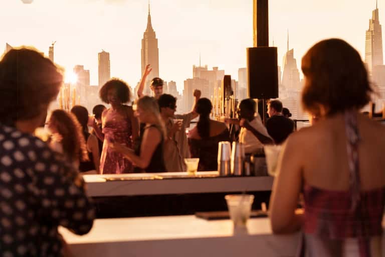 Rooftop bar at sunset with skyline view, attendees at high-top table with drinks