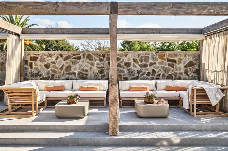 Outdoor seating area with cream cushioned sofas, wooden furniture, and stone accent wall