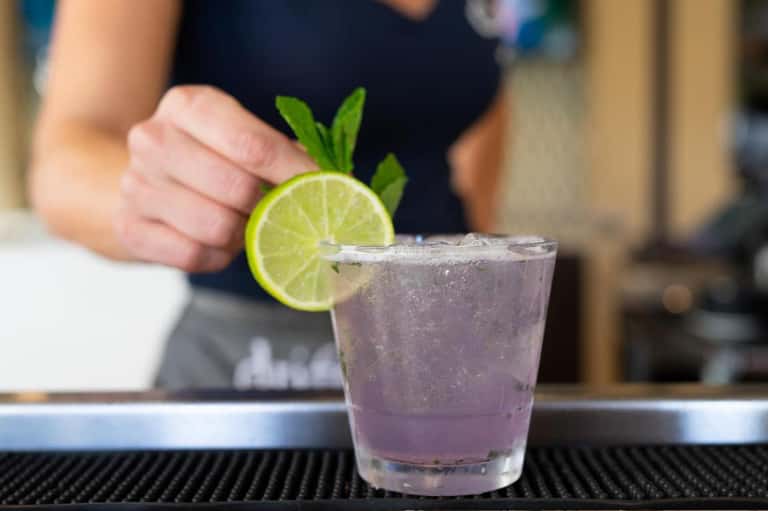 Bartender garnishing cocktail with lime slice and mint on bar counter