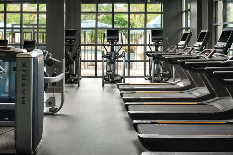 Fitness center with treadmills, stationary bikes, and large windows overlooking outdoor pool area