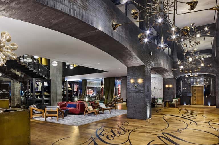 Modern hotel lobby with dramatic lighting, retail shops, red seating, ornate ceiling fixtures, and polished floors