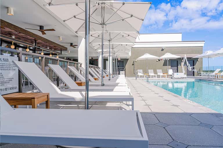 Upscale pool deck with white loungers, umbrellas, lounge chairs, and modern architecture