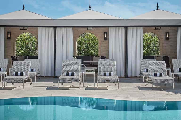 Modern pool cabanas with white umbrellas and striped lounge chairs facing a tranquil blue pool
