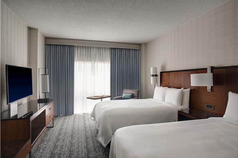 Modern hotel room with two queen beds, flat-screen TV, balcony doors, and contemporary neutral decor
