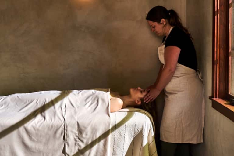 Spa therapist performing massage treatment on client lying on bed in spa room
