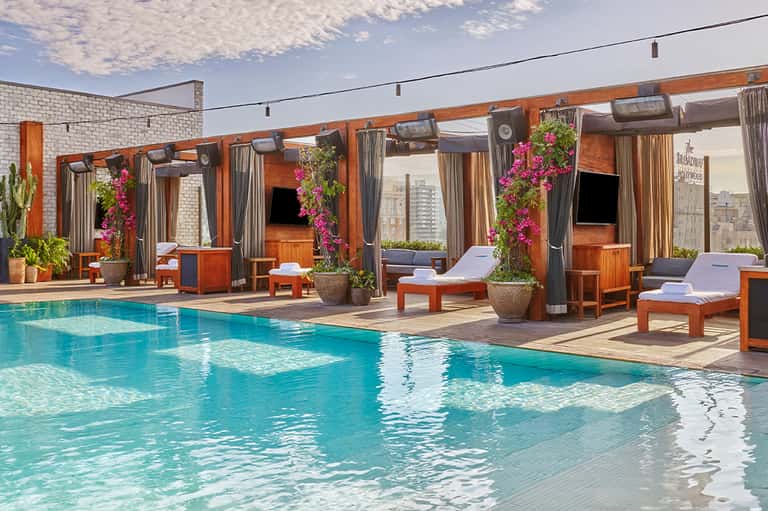 Resort rooftop pool with lounge chairs, wooden cabanas, and city skyline views