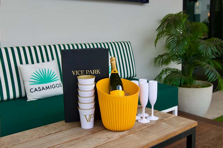 Vice Park branding with champagne bottle in yellow bucket, green striped seating, and palm plant accents