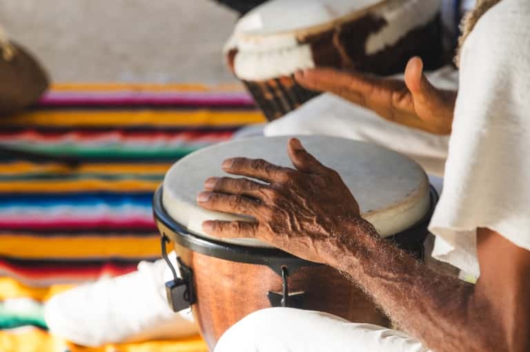 Hands playing traditional drums on colorful woven textile background