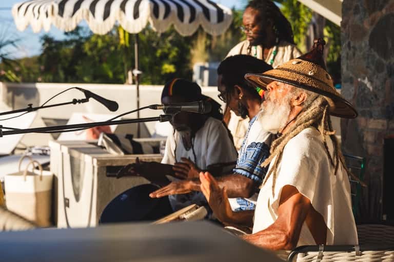 Musicians performing at an outdoor poolside event under a striped umbrella