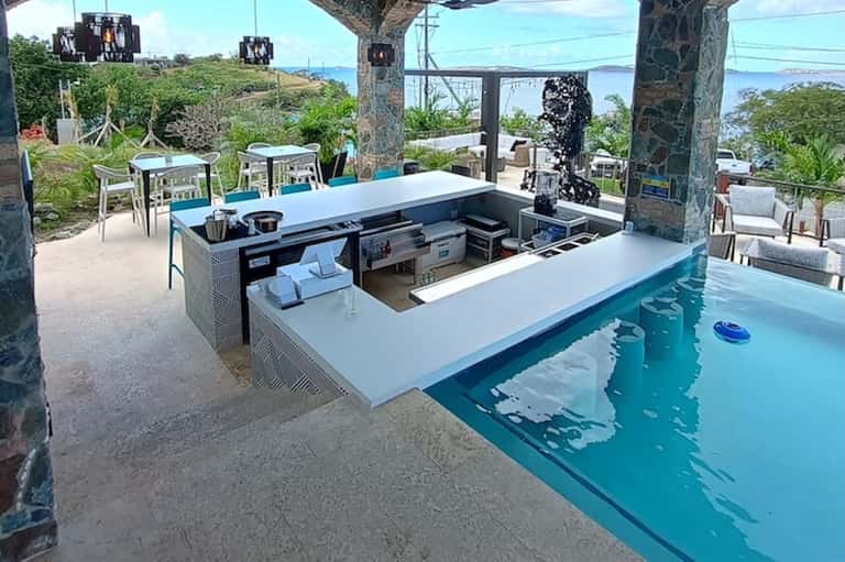 Clifftop pool bar with ocean views, white counter seating, and tropical vegetation surrounding the turquoise water