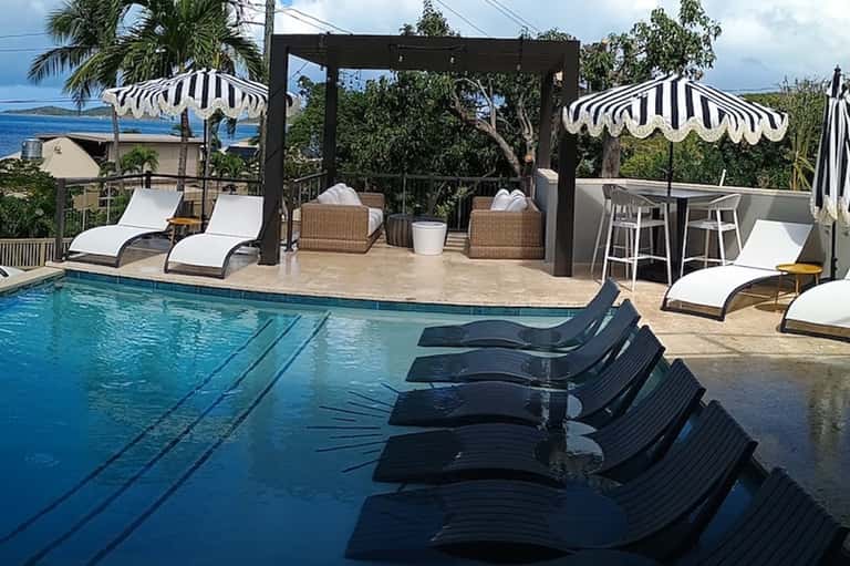 Resort pool area with black loungers, striped umbrellas, bar seating, and ocean view