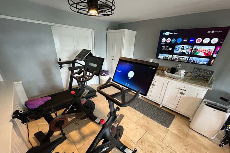 Home gym with exercise bikes, treadmill, and large TV screens on wall