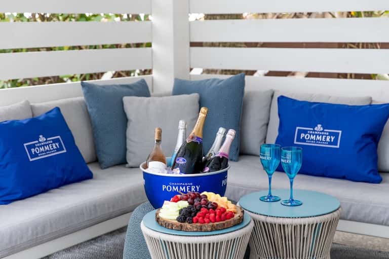 Luxury poolside lounge with champagne setup, fruit tart, Pommery branded pillows, and elegant seating arrangement