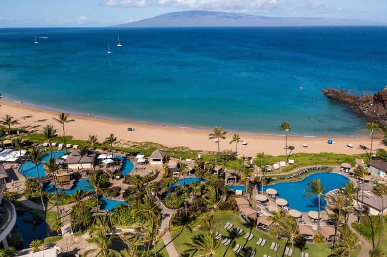 Aerial view of tropical beach resort with multiple blue pools, palm trees, and turquoise ocean