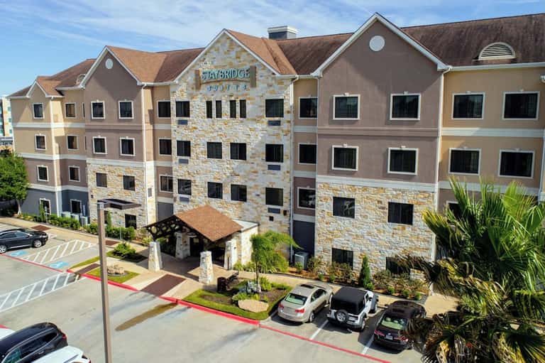 StayBridge hotel exterior with multi-story stone and tan facade, parked cars, and entry canopy