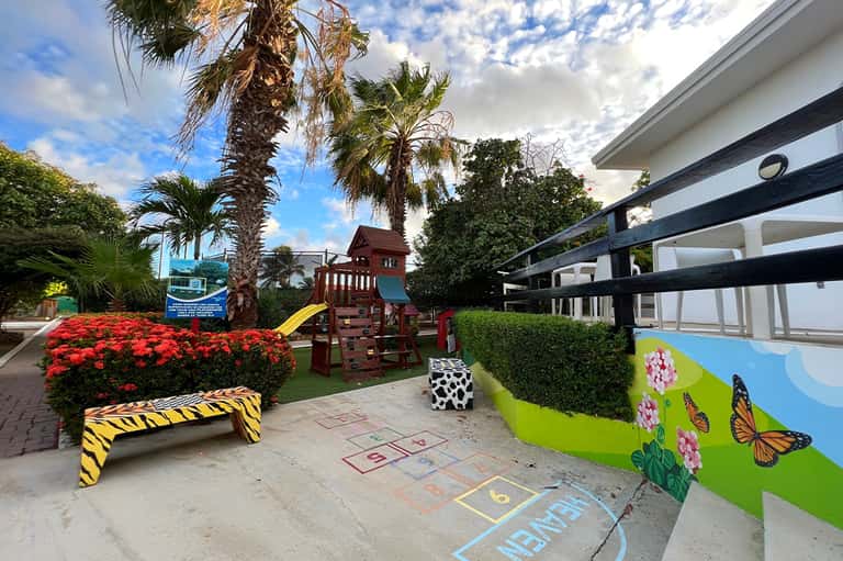 Children's play area with colorful playground equipment, flower mural, and palm trees