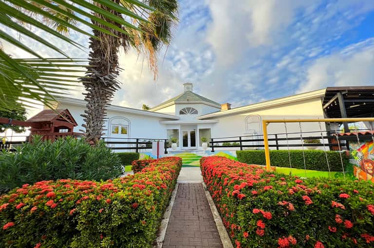 Resort entrance with brick pathway, red flower gardens, and white main building