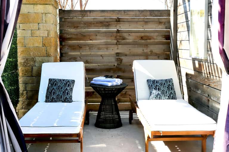 Private patio with two white lounge chairs, black side table, and wooden steps