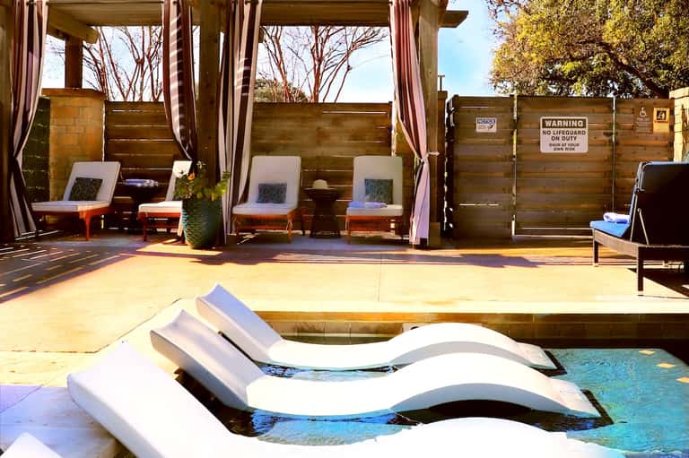 Poolside cabanas with purple striped curtains, cushioned loungers, and wooden privacy screens
