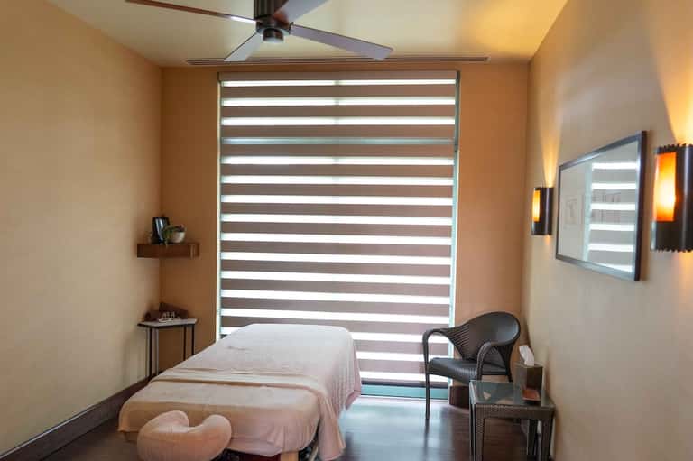 Minimalist spa treatment room with massage bed, striped window blinds, and modern decor