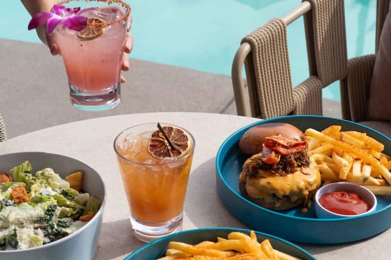 Poolside dining with cocktail, burger and fries, salad, and ocean view background