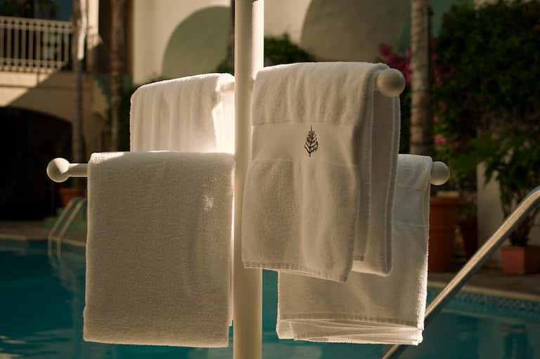 White embroidered resort towels hanging on rail overlooking poolside patio and greenery