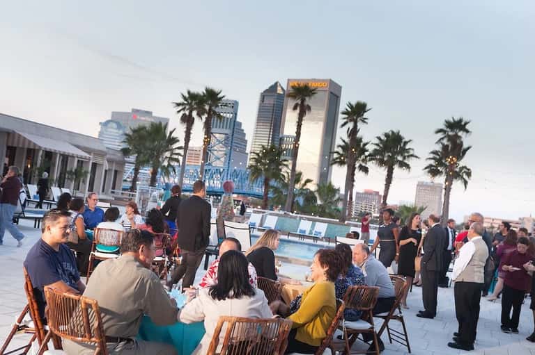 Rooftop event with guests mingling near pool overlooking city skyline and palm trees
