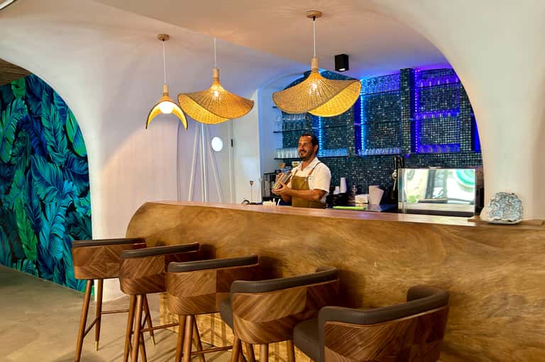 Modern hotel bar with curved wooden counter, golden pendant lights, and city skyline view