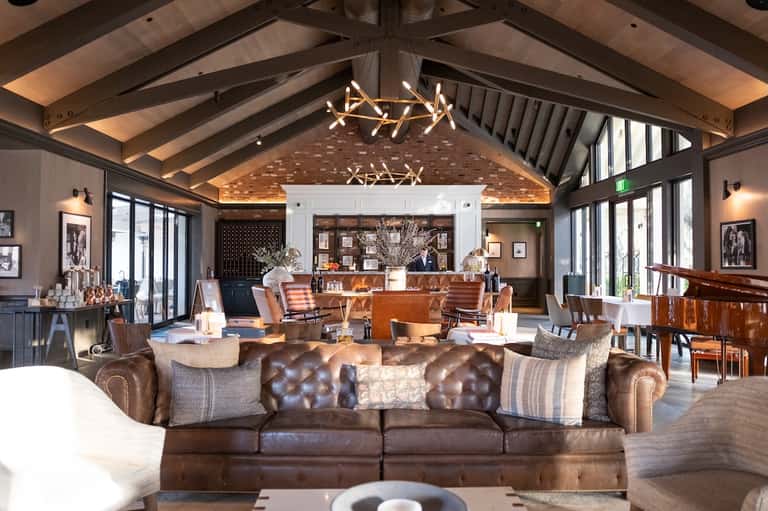 Spacious resort lobby with exposed wood ceiling beams, leather seating, fireplace, and modern chandelier
