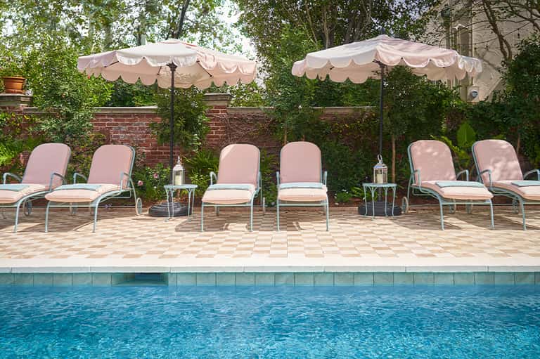 Poolside seating area with pink umbrellas, lounge chairs, brick wall, and evergreen landscaping