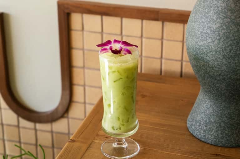 Green matcha beverage in tall glass garnished with purple orchid flower