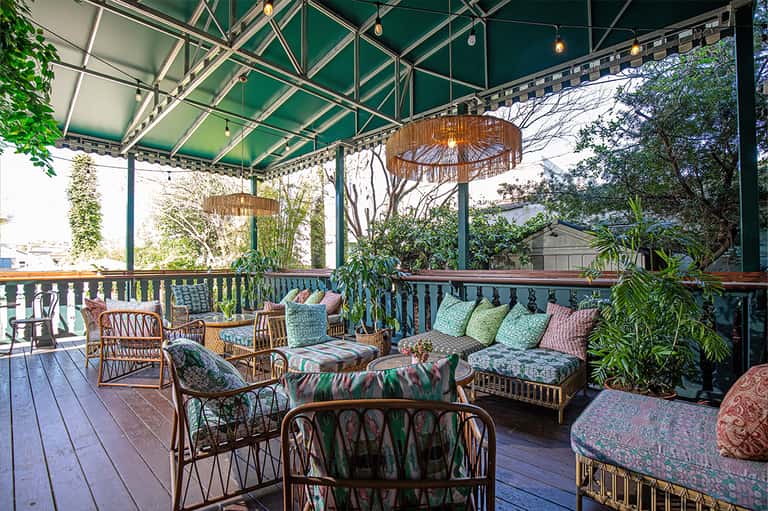 Covered outdoor patio with rattan furniture, colorful cushions, and lush green plants