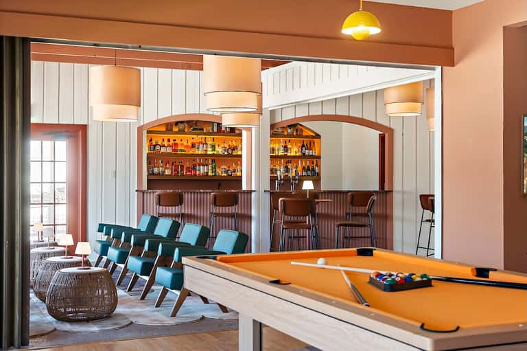 Hotel recreation room with billiards table, bar area with stocked shelves, and lounge seating