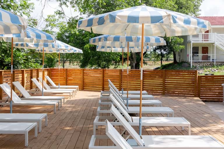 Outdoor deck lounge with white loungers, blue and white striped umbrellas, and wooden privacy screens