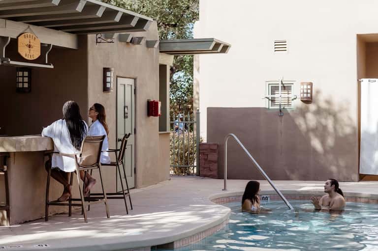 Resort hot tub area with bar counter, guests in spa water, desert landscaping, and minimalist architecture