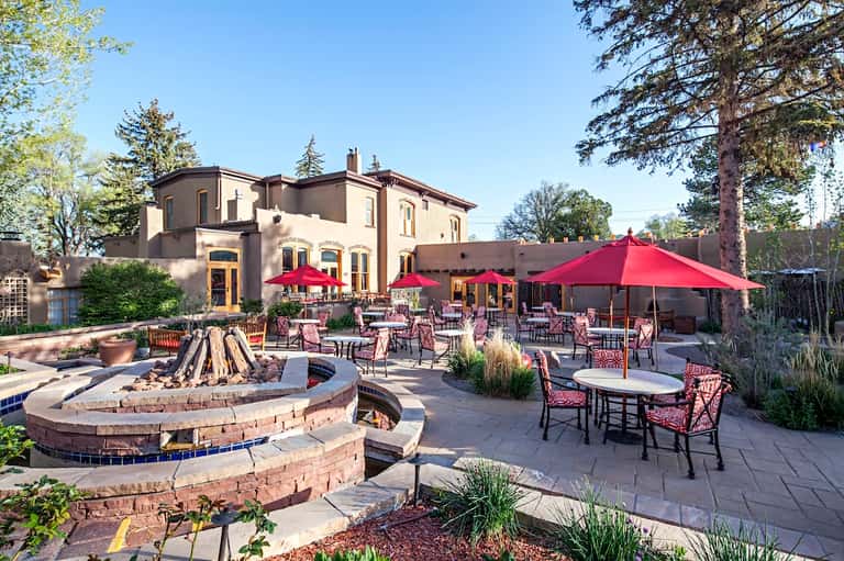 Resort courtyard with fire pit, red umbrellas, dining tables, and historic mansion building