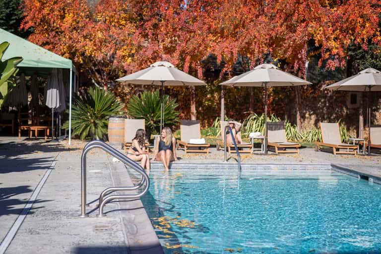 Outdoor pool with white umbrellas, lounge chairs, and red autumn foliage backdrop at resort