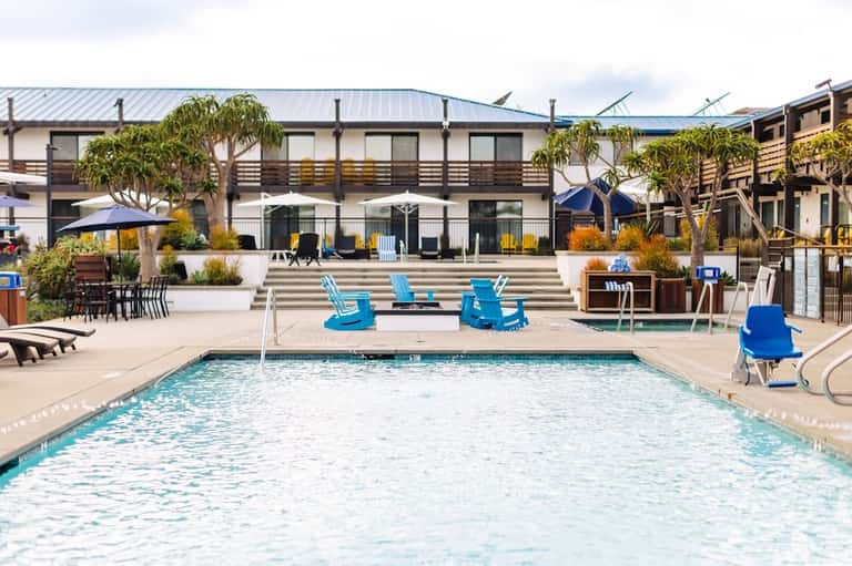 Resort pool with blue Adirondack chairs, cabanas, and modern lodge-style building