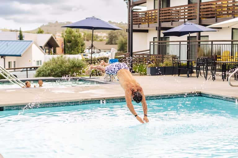 Guest diving into outdoor swimming pool with hot tub, umbrellas, and hillside resort views