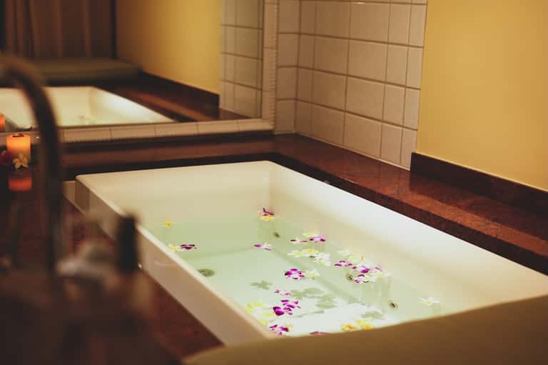Spa bathtub filled with green water and floating flower petals, with ambient candlelight