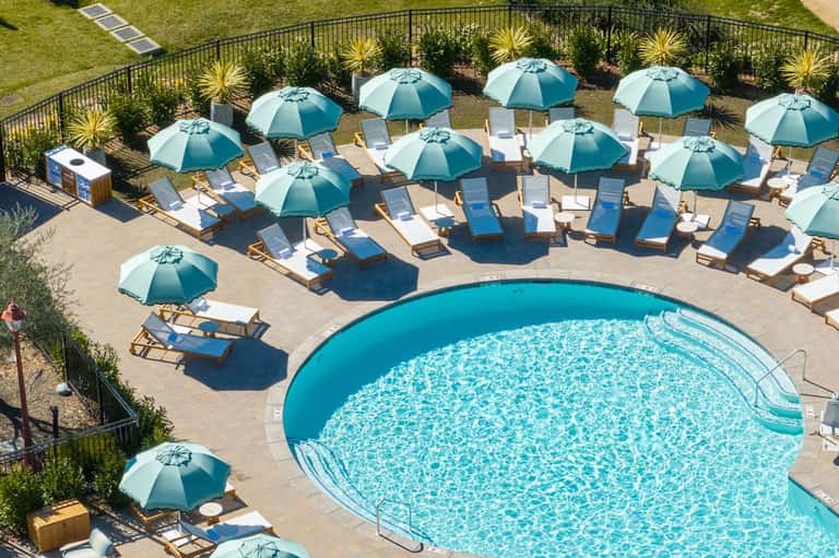 Resort pool surrounded by teal umbrellas and lounge chairs with landscaped lawn area