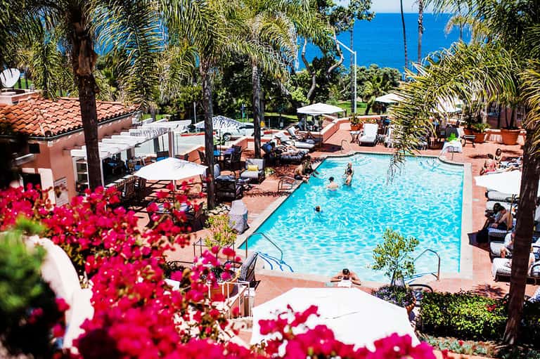 Resort pool surrounded by pink buildings, palm trees, and vibrant bougainvillea flowers