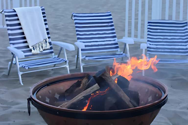 Fire pit on waterfront deck with navy striped lounge chairs and calm bay water in background